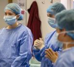 Pupils wear blue scrubs, masks, and caps stand attentively indoors, conveying focus and teamwork in a medical setting.