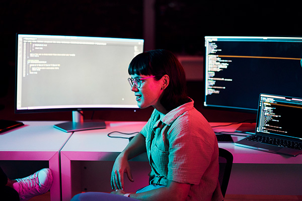 Woman sitting in front of computers developing practical solutions in code.
