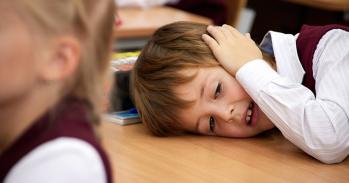 In a classroom, a tired boy is resting on a desk
