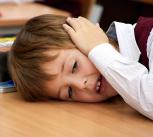 In a classroom, a tired boy is resting on a desk