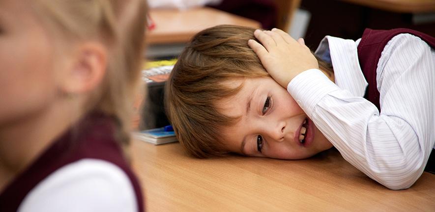 In a classroom, a tired boy is resting on a desk