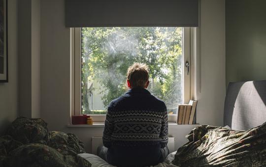 Anxious man looking out of his bedroom window on a sunny day