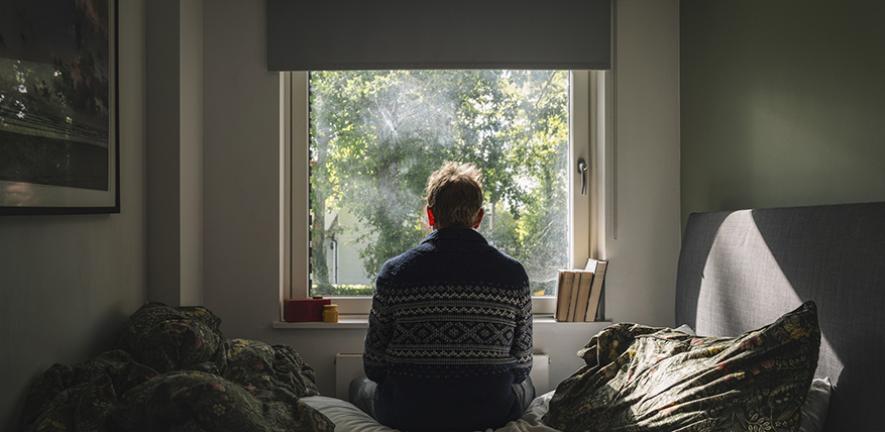 Anxious man looking out of his bedroom window on a sunny day
