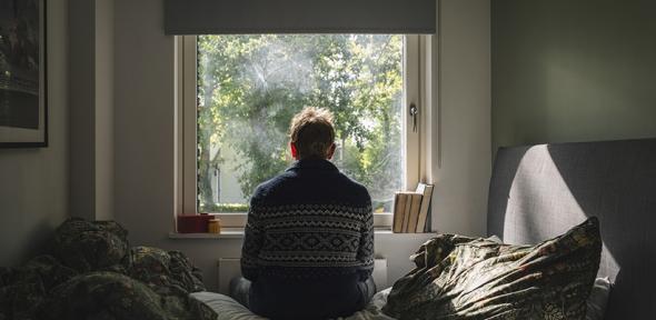 Anxious man looking out of his bedroom window on a sunny day