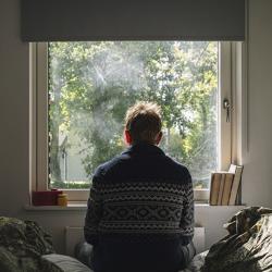 Anxious man looking out of his bedroom window on a sunny day