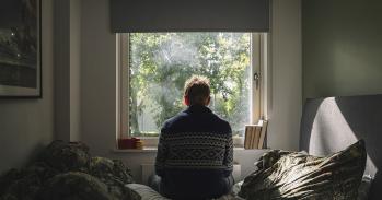 Anxious man looking out of his bedroom window on a sunny day