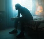 Man in black jacket sitting on bed