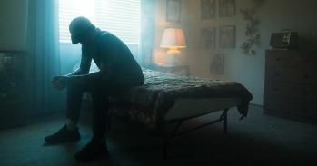 Man in black jacket sitting on bed