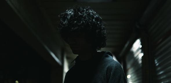 A man standing in a dark hallway with his hands in his pockets