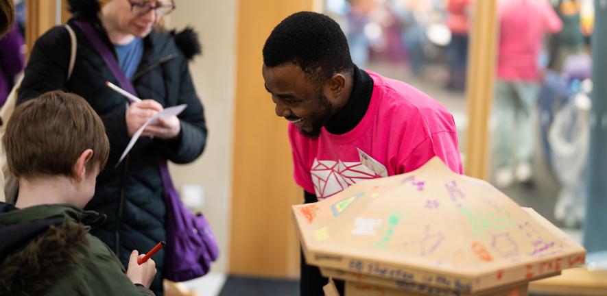 A volunteer smiles at children drawing next to a cardboard hand-decorated post box.